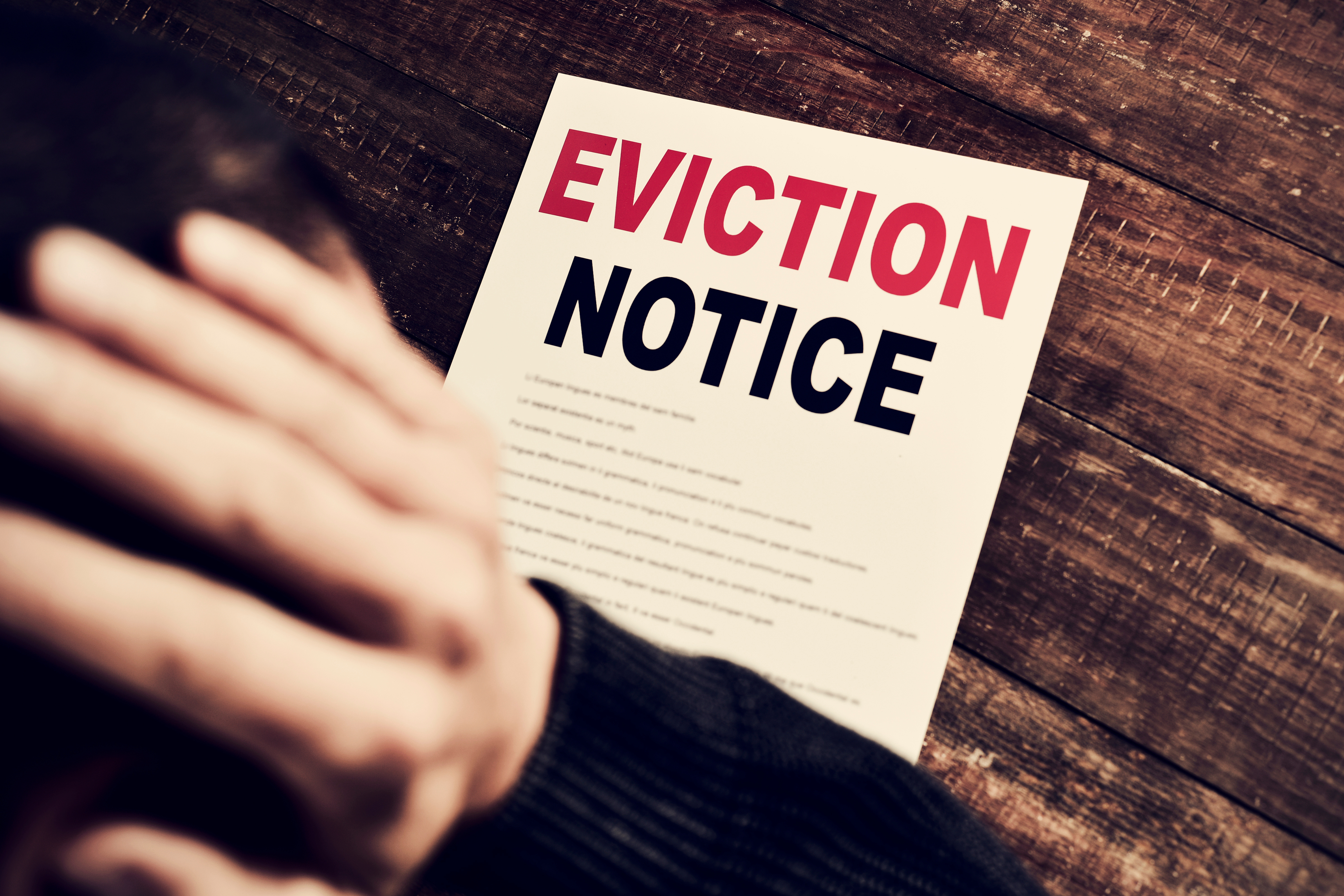 A person holding their head in distress with an eviction notice on the table.