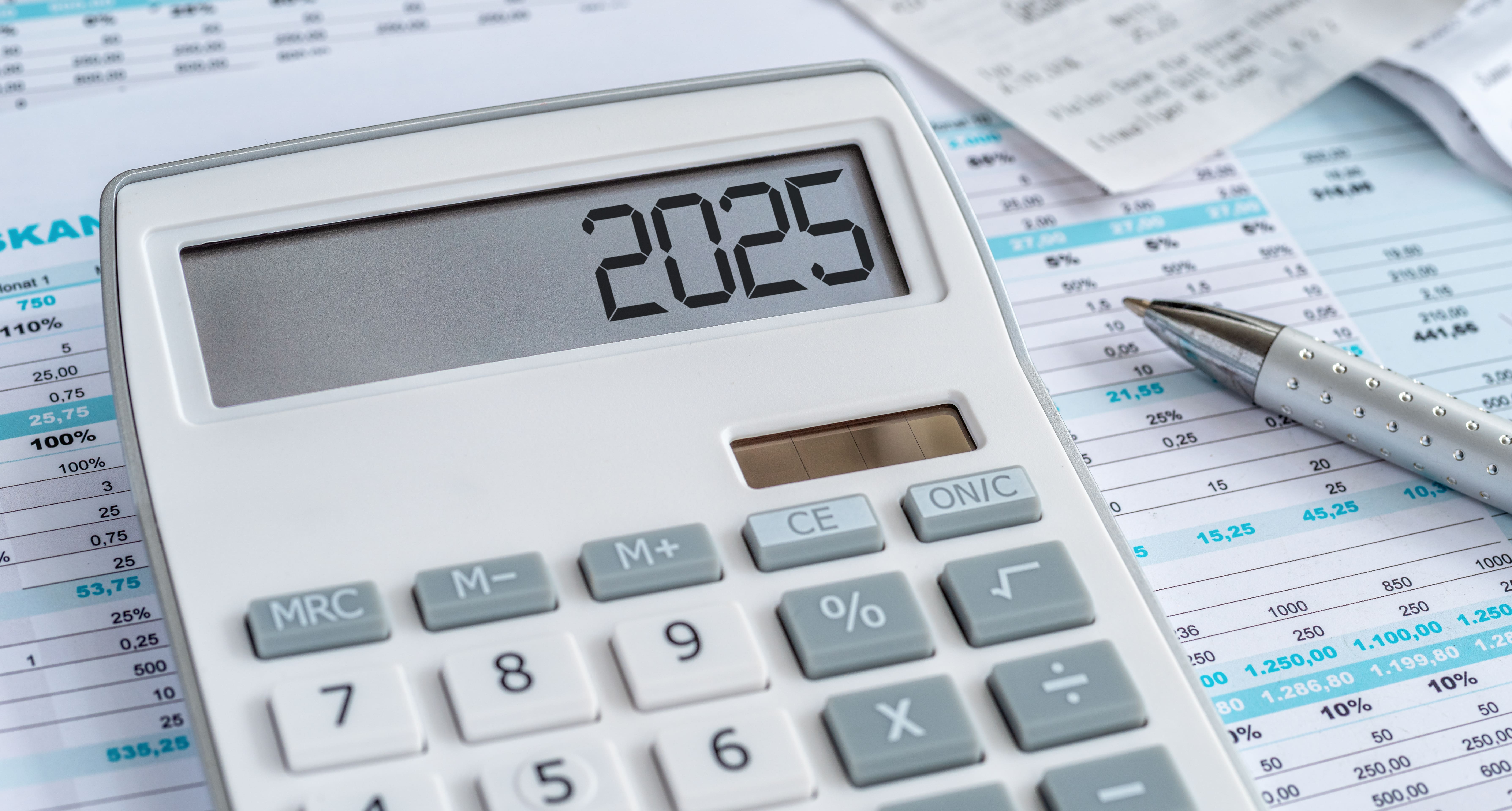 Calculator displaying ‘2025’ with financial spreadsheets and a pen in the background, referencing real estate investment planning for the year 2025.