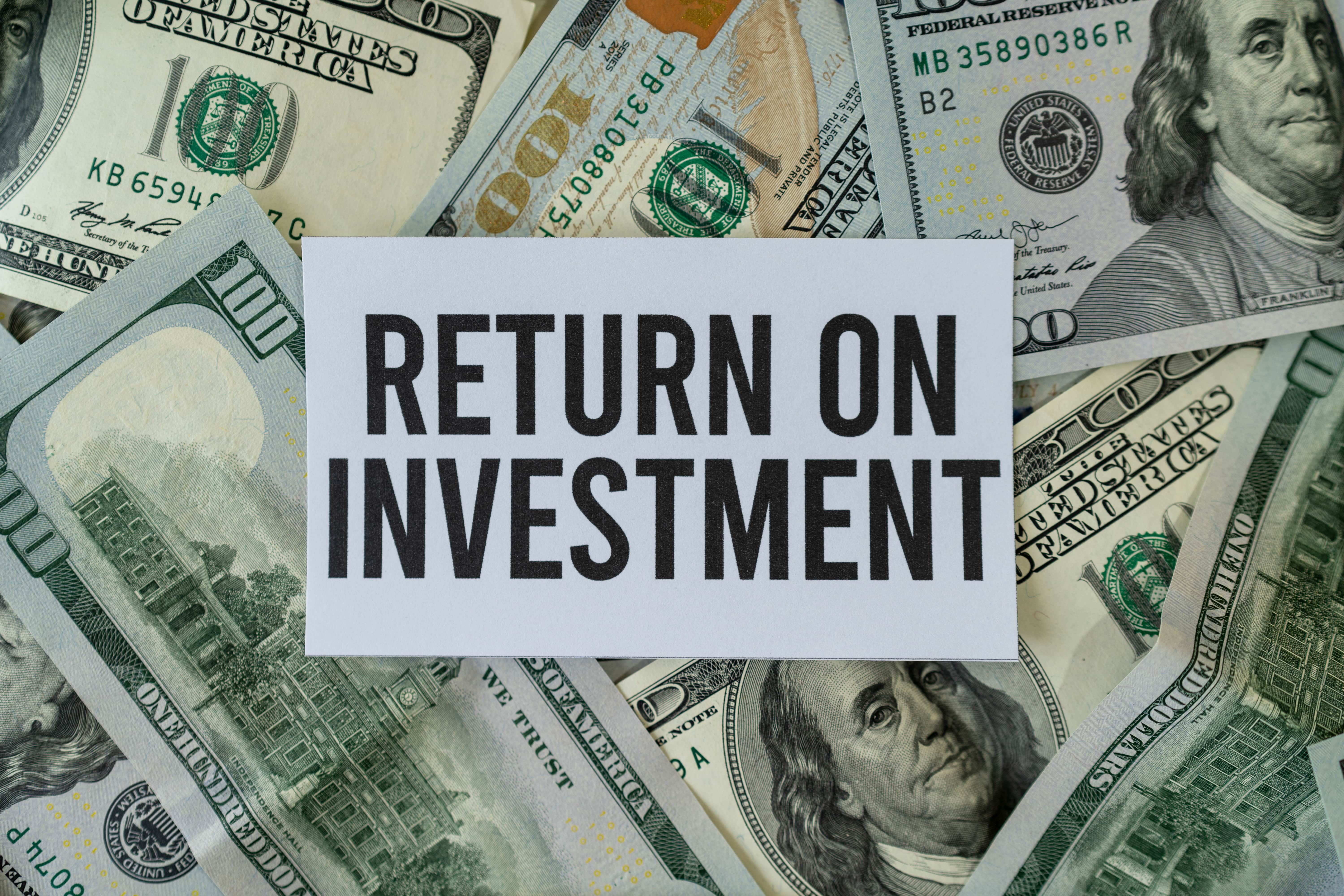 Sign reading ‘Return on Investment’ surrounded by U.S. hundred-dollar bills, highlighting the financial goals of BRRRR investing.