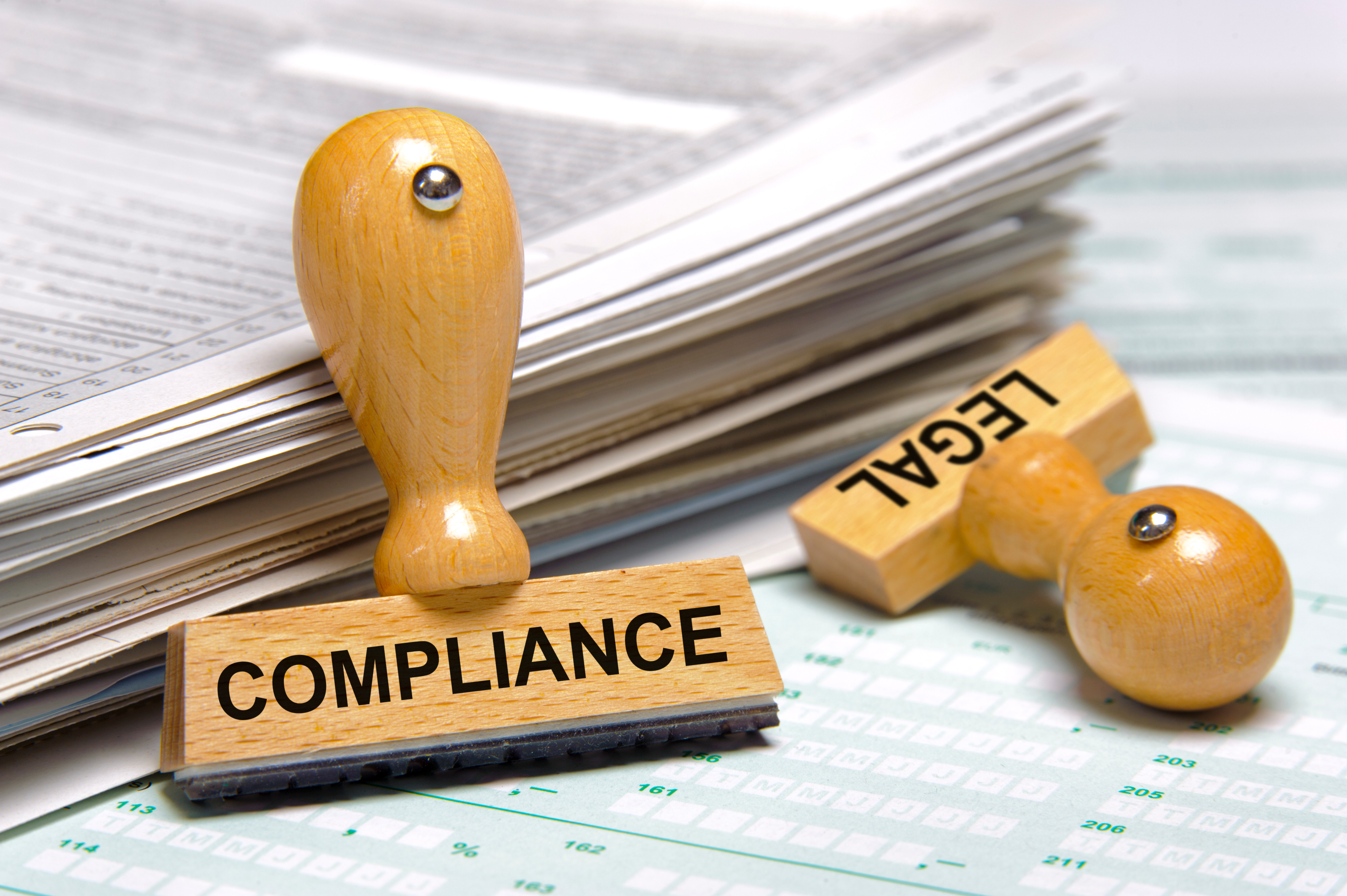 Close-up image of wooden compliance and legal stamps on top of paperwork, symbolizing adherence to regulations and legal requirements.