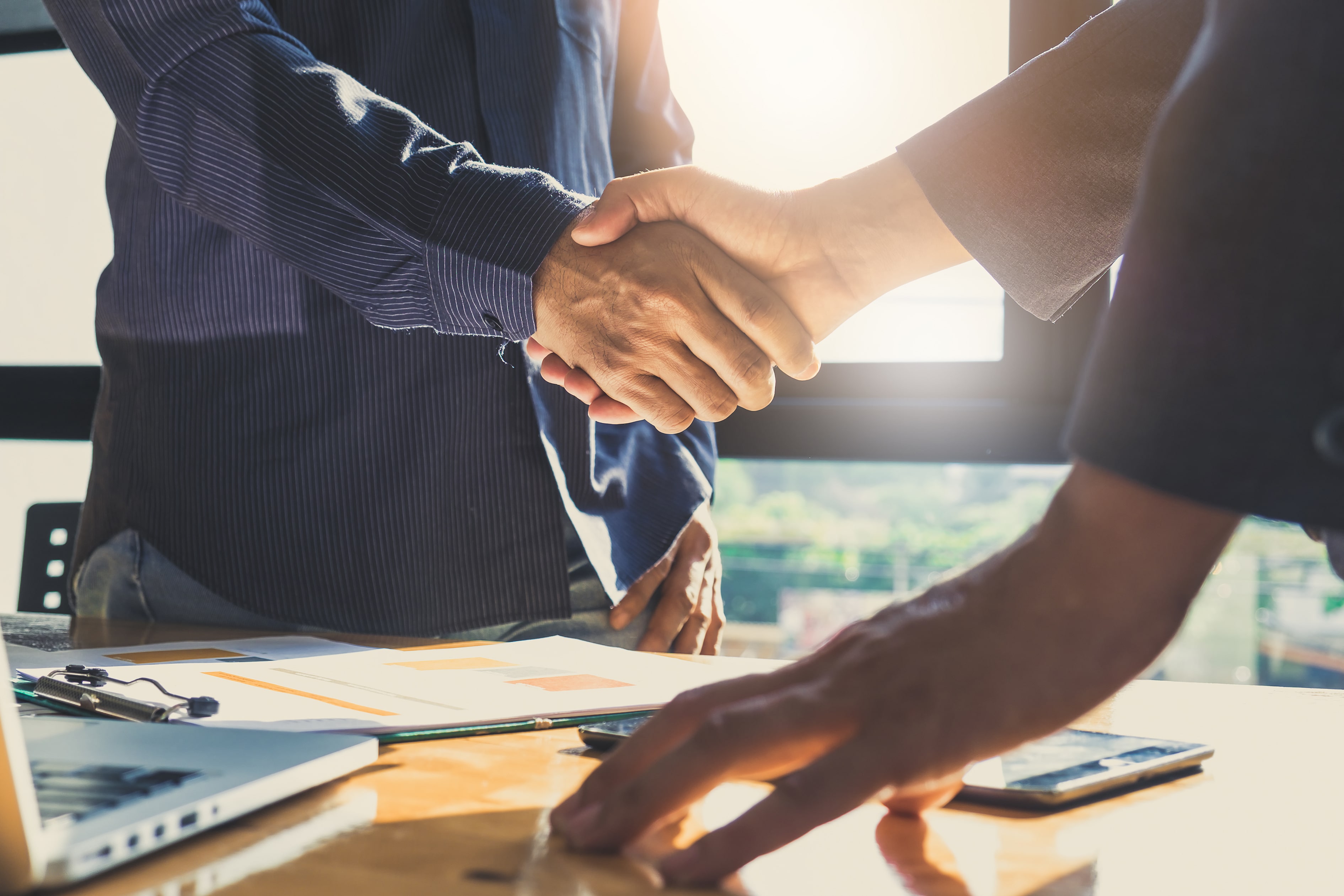 Two business professionals shaking hands over a table with documents and laptops, symbolizing a successful rental property deal.