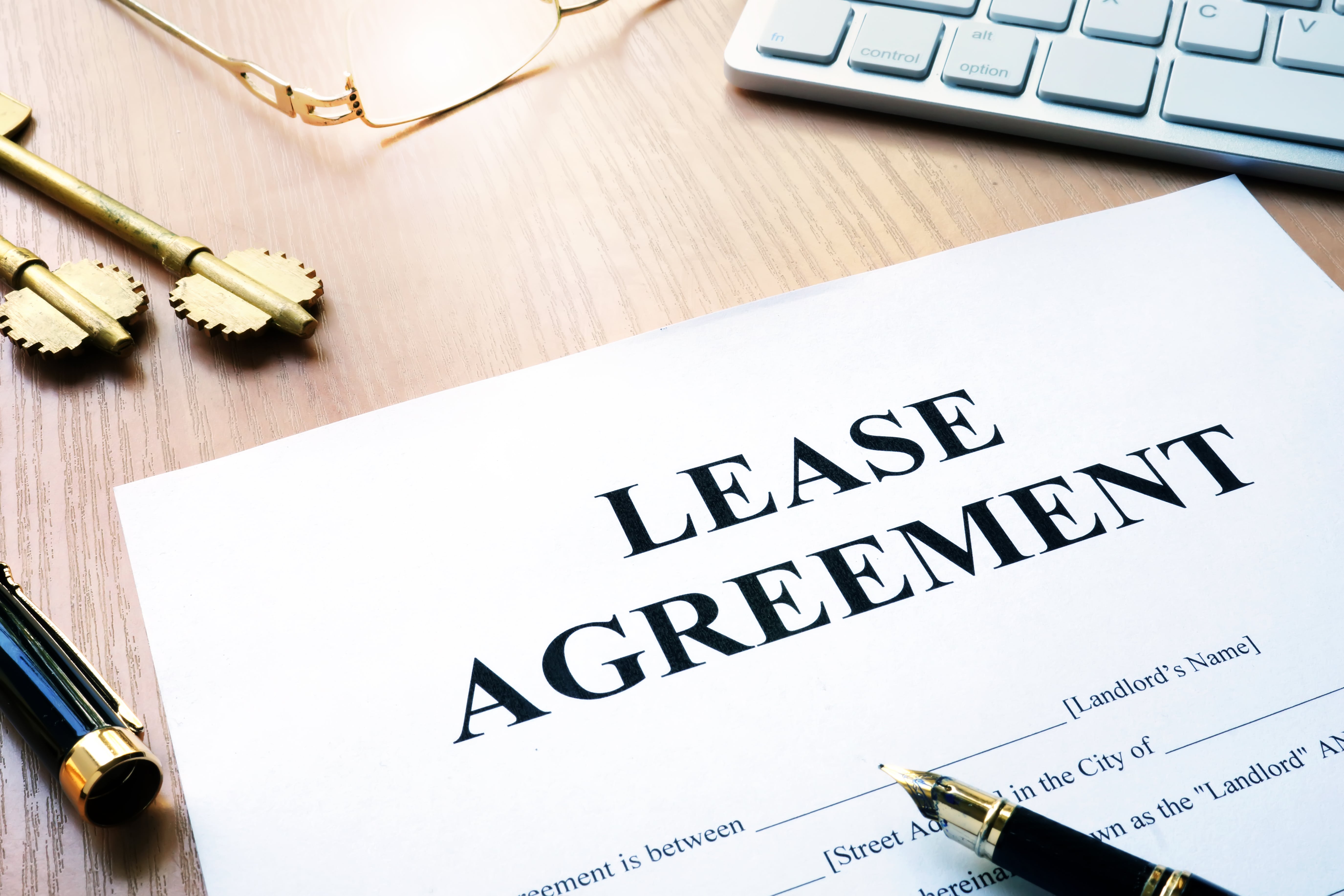 Paper lease agreement with pen, antique keys, and eyeglasses on a wooden desk—symbolizing formal long-term rental contracts.