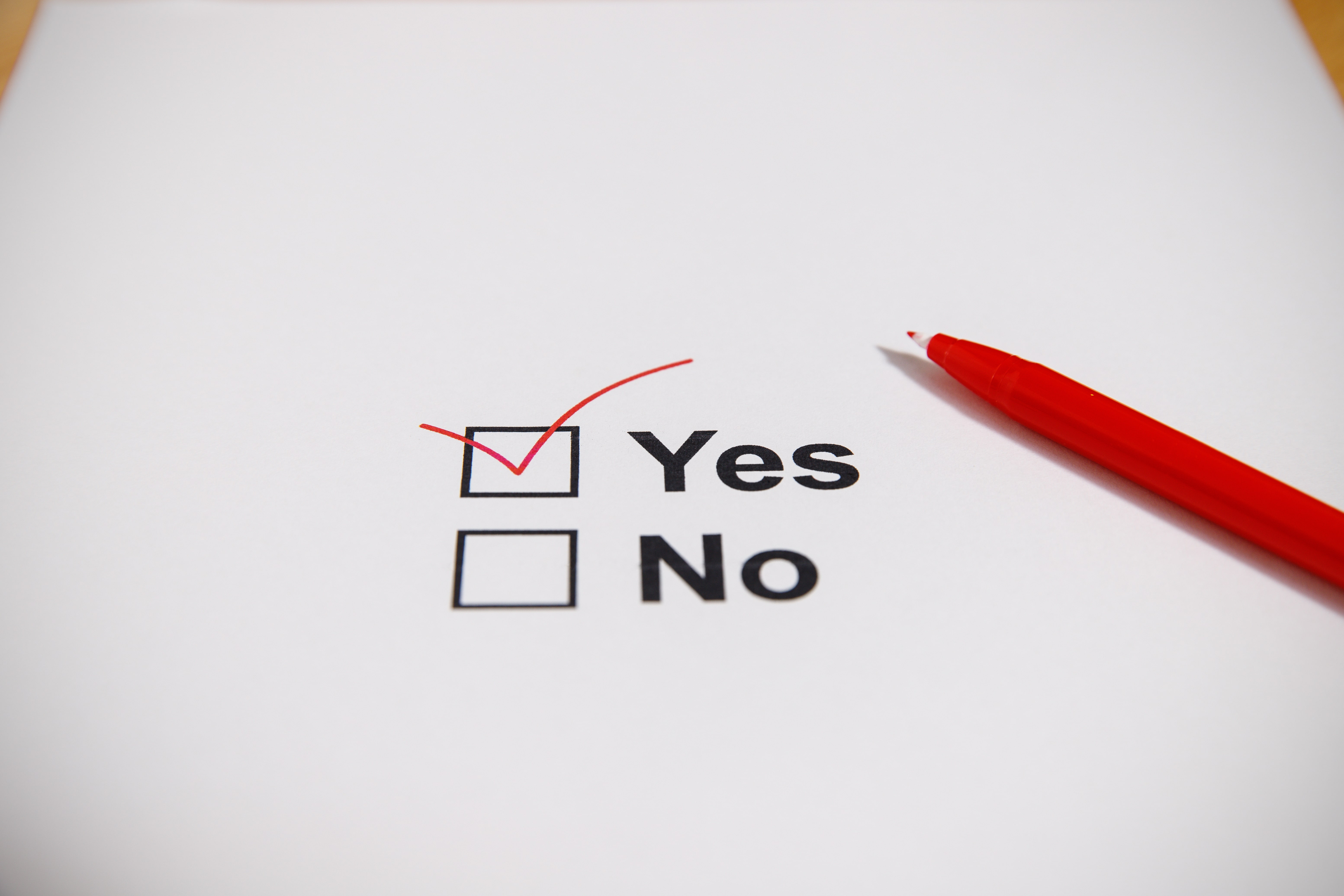 A close-up of a checklist with 'Yes' marked in red ink and a red pen beside it, symbolizing decision-making and commitment.