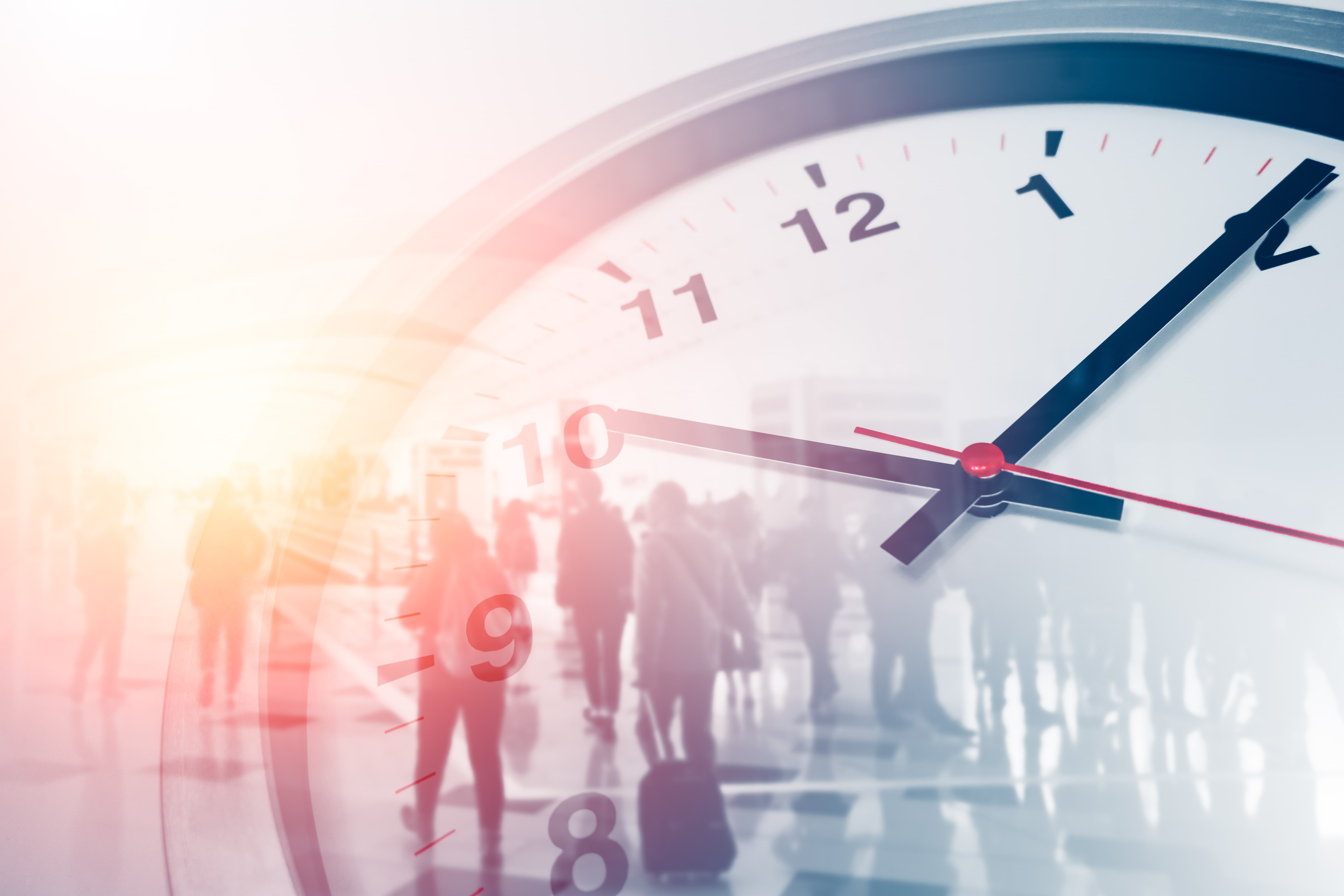 Close-up of a large clock with a blurred crowd of people in the background, representing time management and the fast-paced nature of daily life.