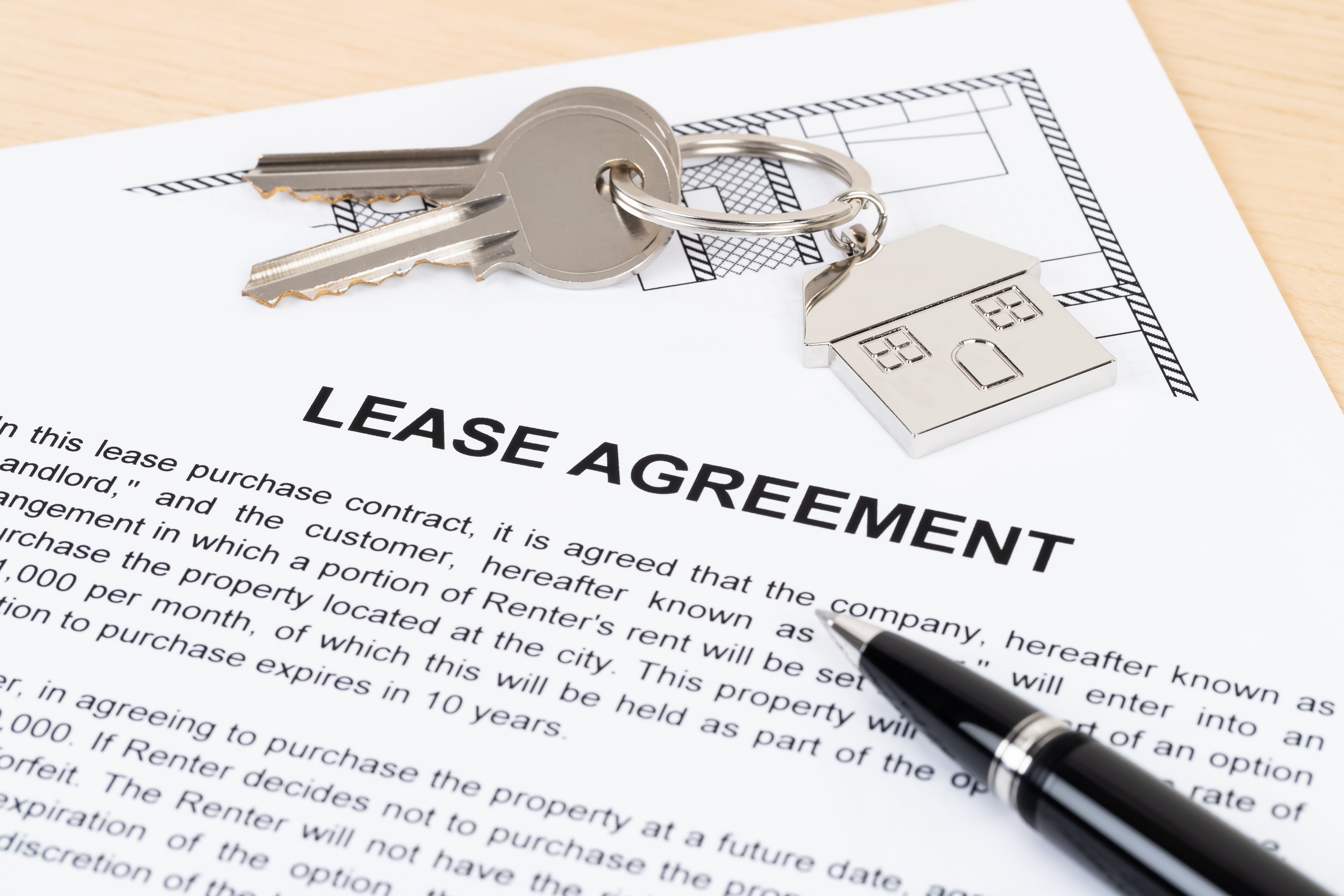 A lease agreement document with house keys and a keychain in the shape of a home, representing the rental process.