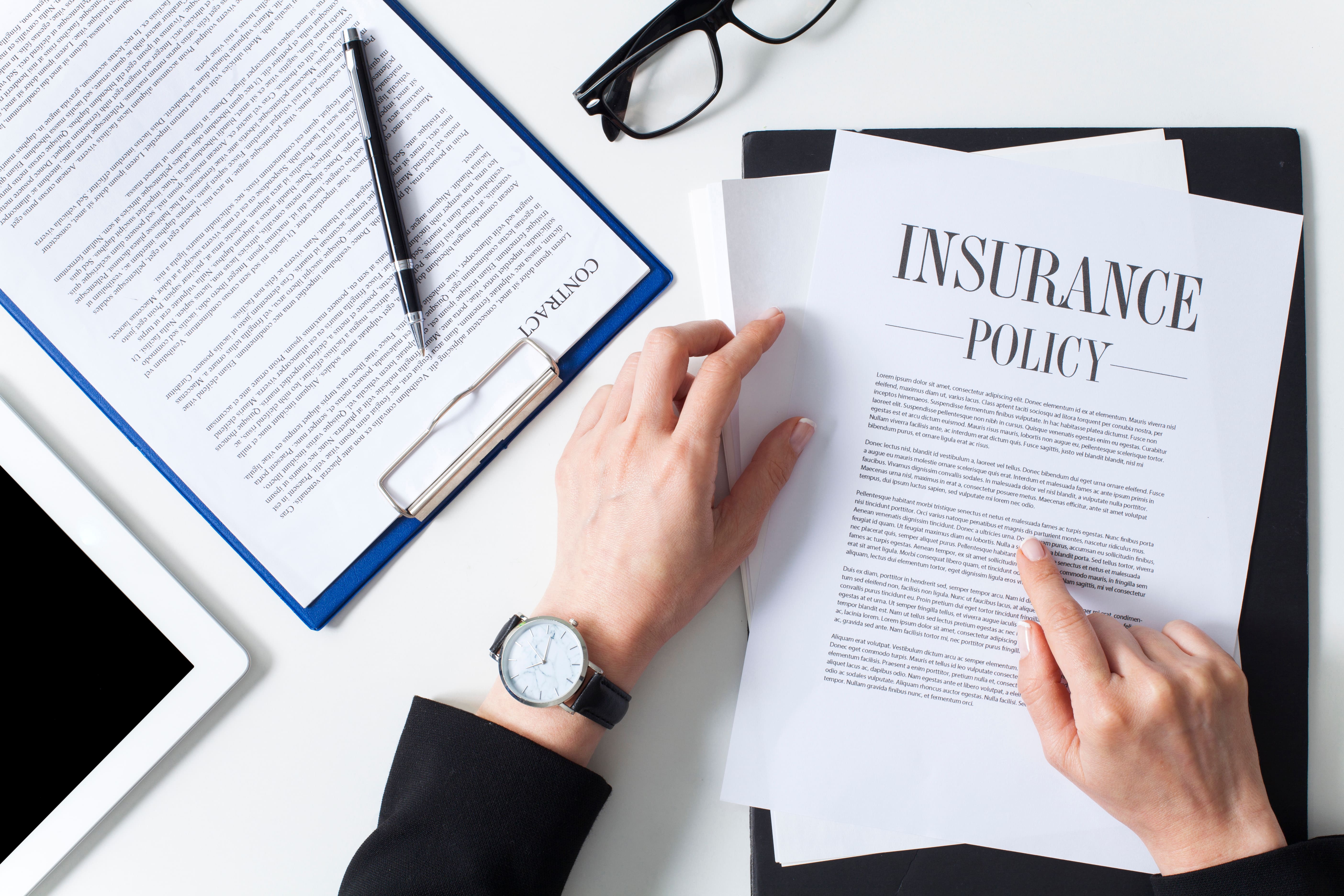 Person reading an insurance policy document at a desk with contracts, glasses, and a digital tablet—highlighting landlord coverage needs.