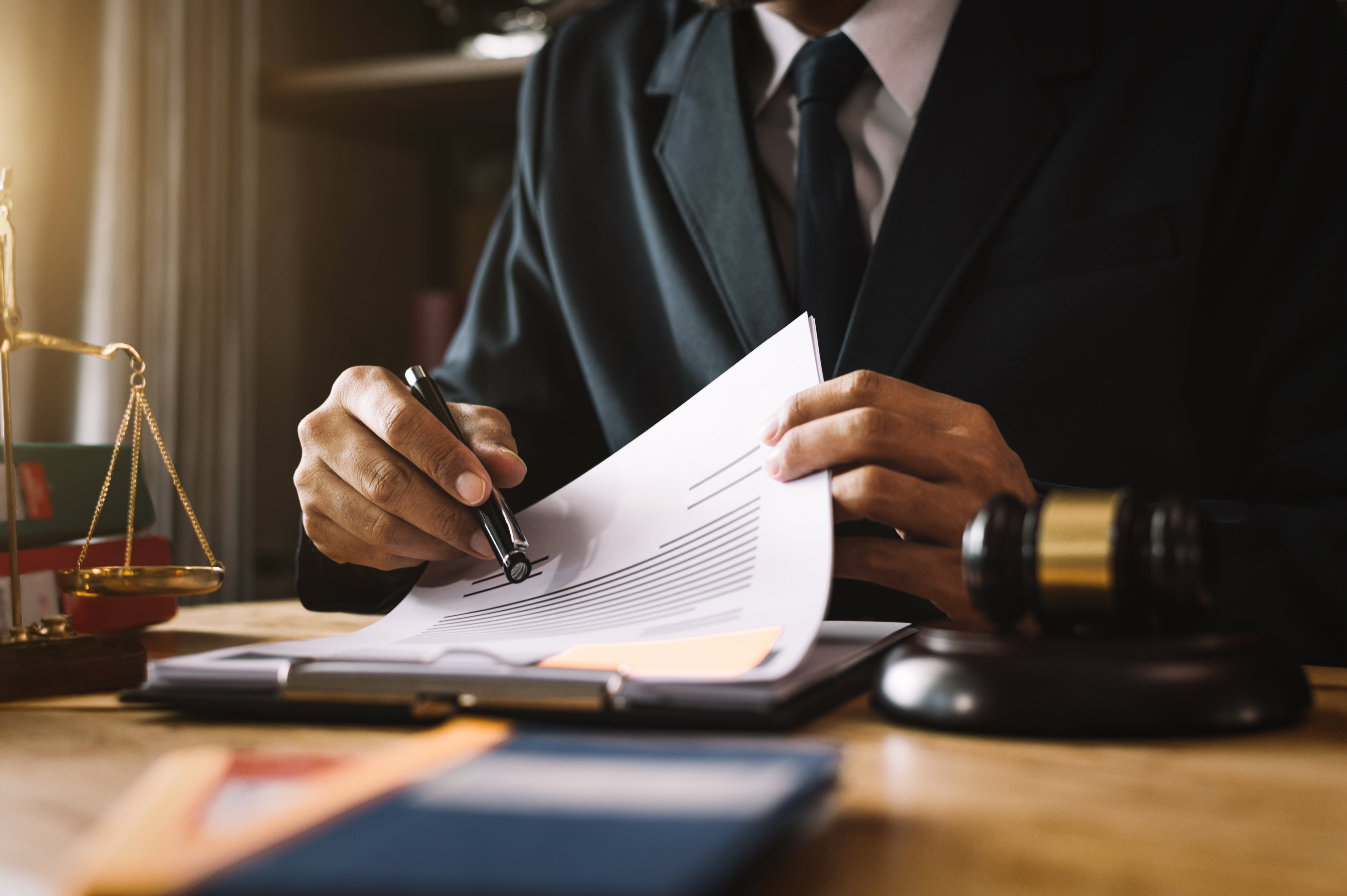 Close-up of a suited attorney reviewing rental regulations and lease compliance documents at a desk with a gavel and scales.