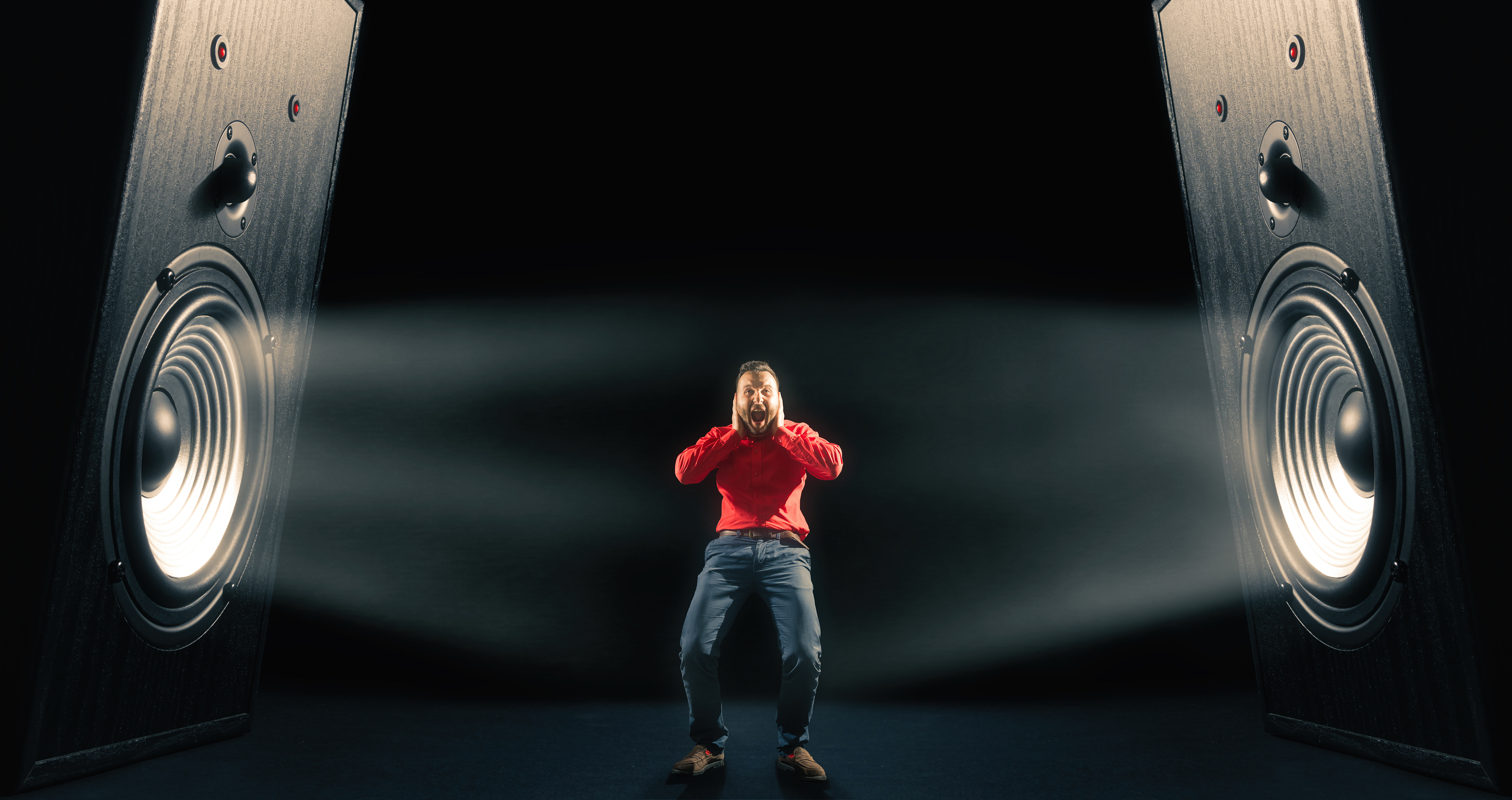 A man overwhelmed by loud noise, holding his head between two large speakers.