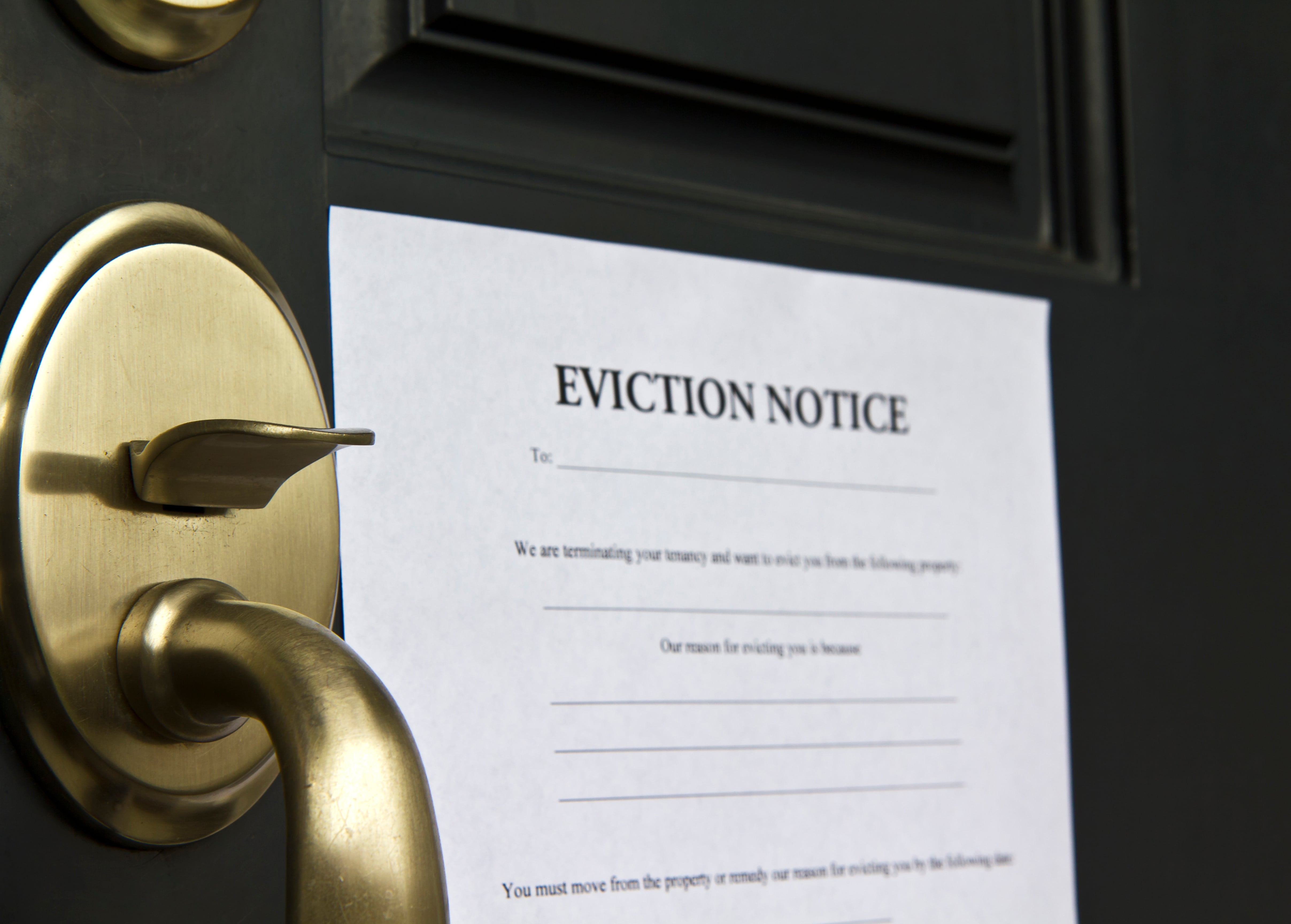 An eviction notice taped to a front door with a brass doorknob, indicating a formal tenant notification.