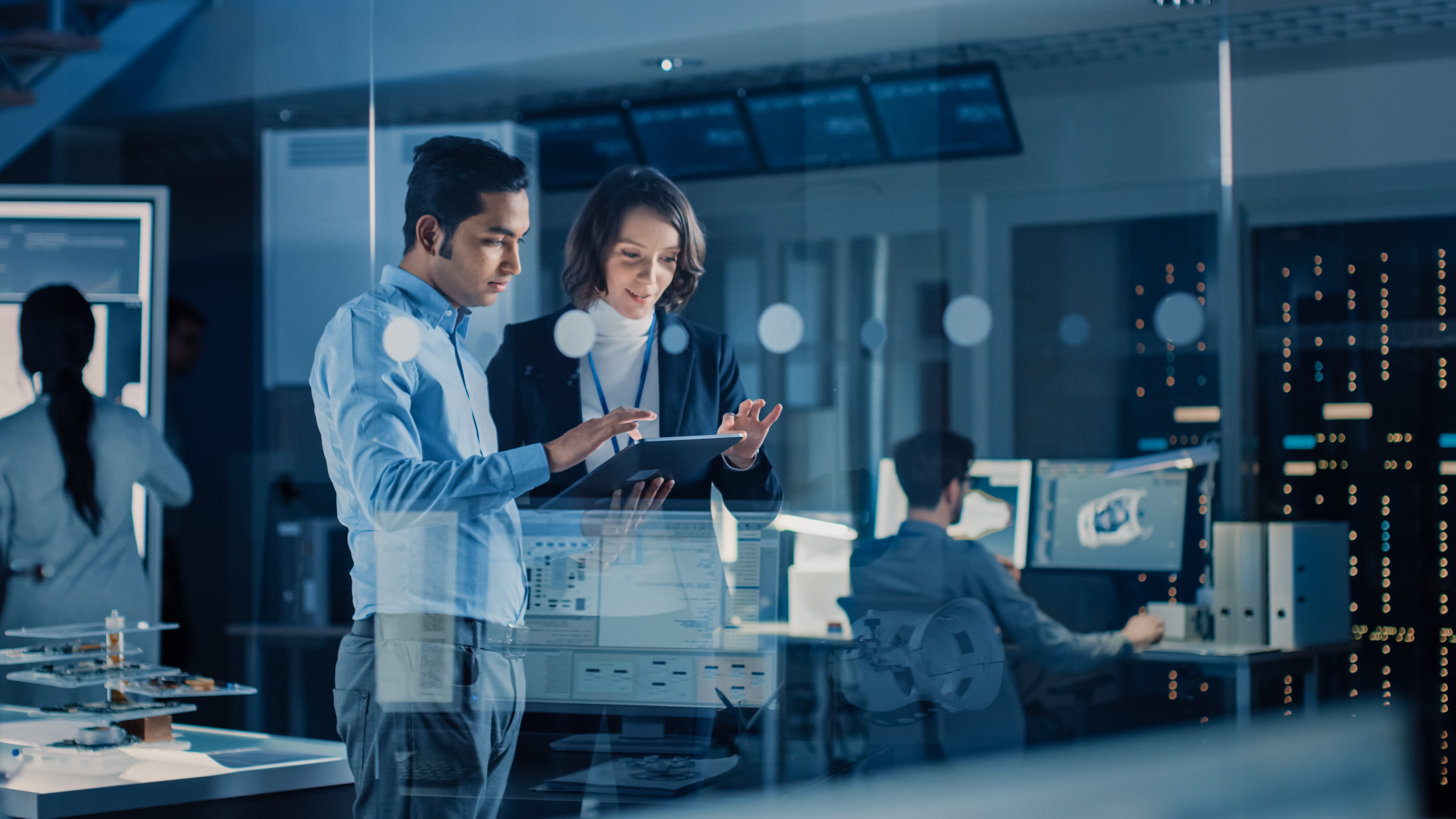 Tech professionals collaborating in a modern high-tech office, surrounded by advanced screens and equipment.