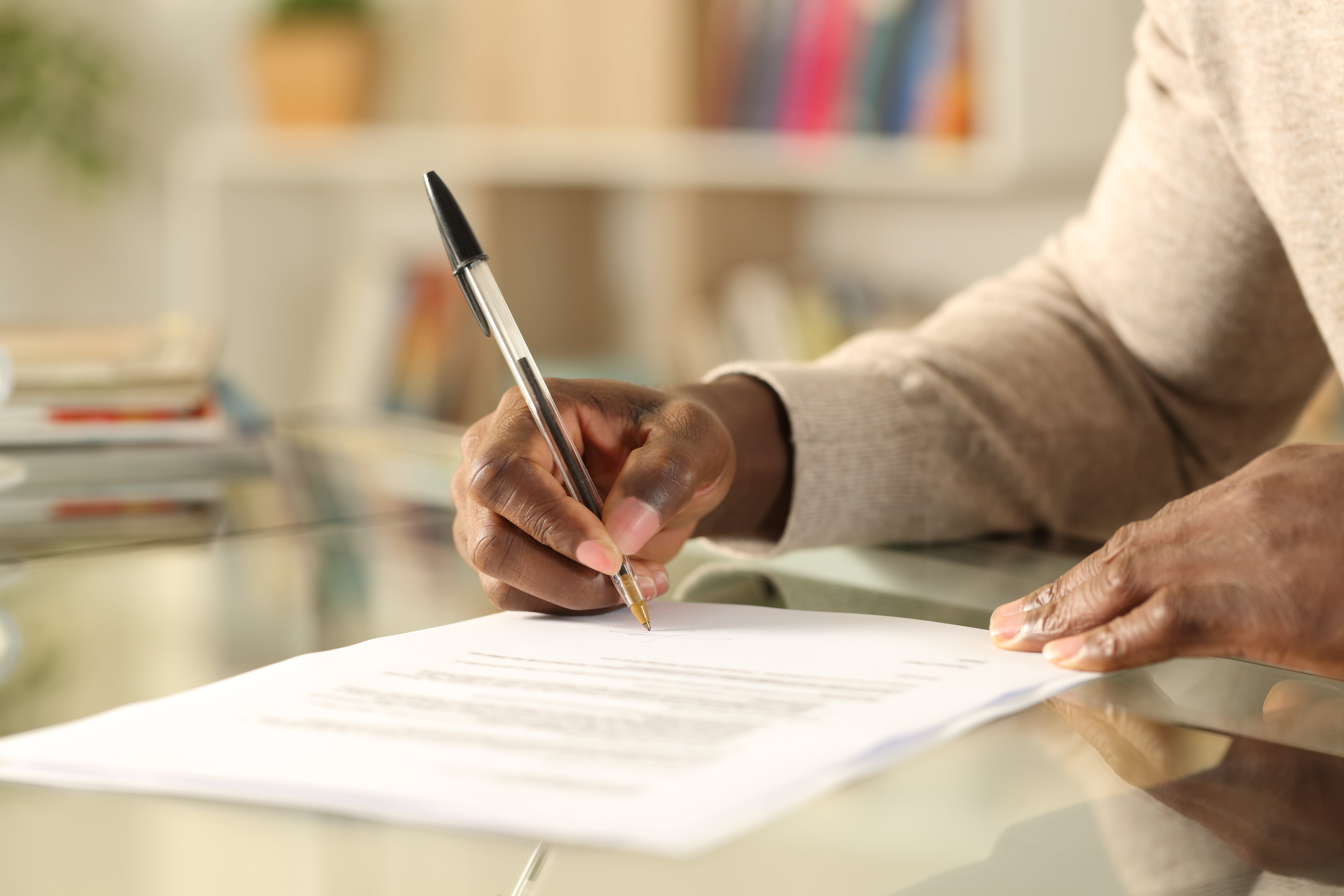 A close-up of a person’s hand holding a pen while signing a document. The scene suggests an important contract or agreement, possibly related to a real estate or rental transaction.