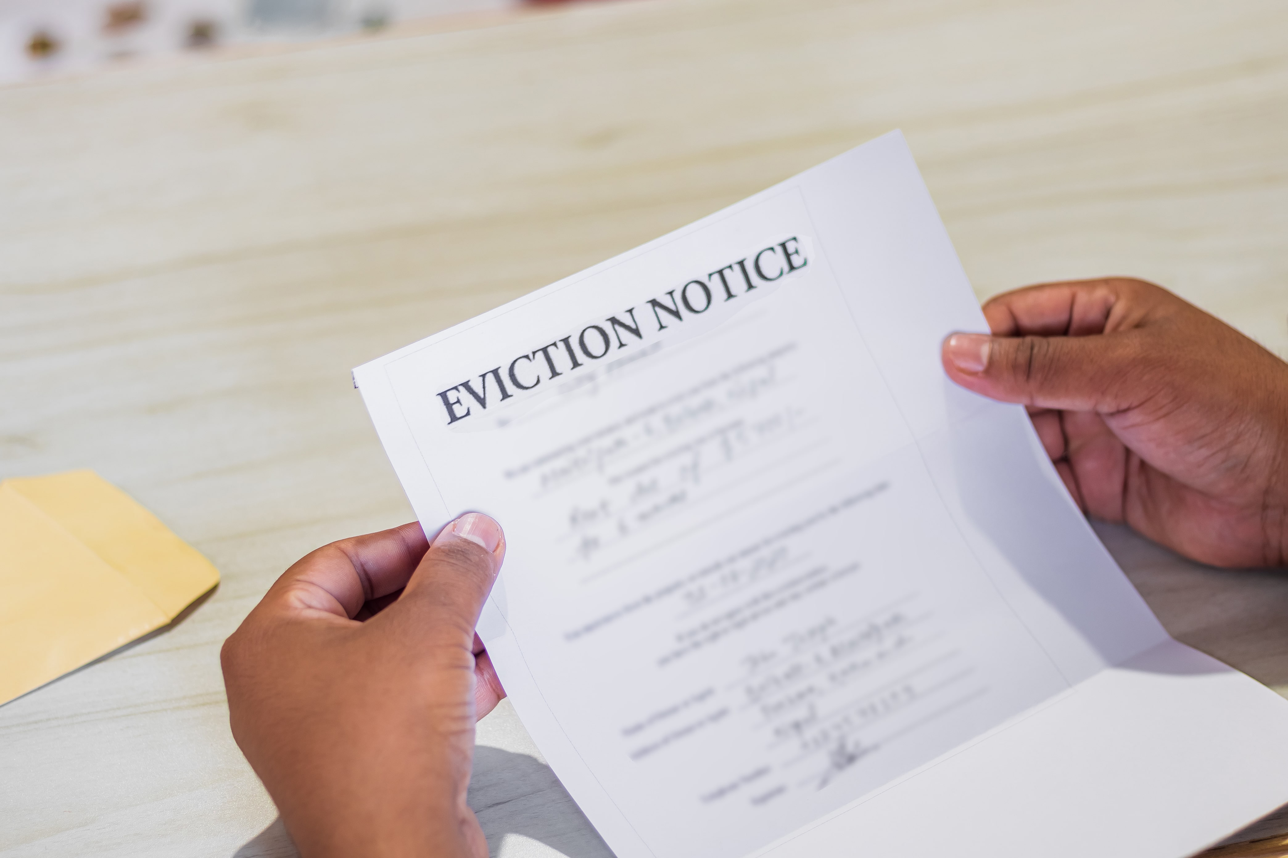 Hands holding an eviction notice inside an envelope, symbolizing the legal process of notifying tenants.