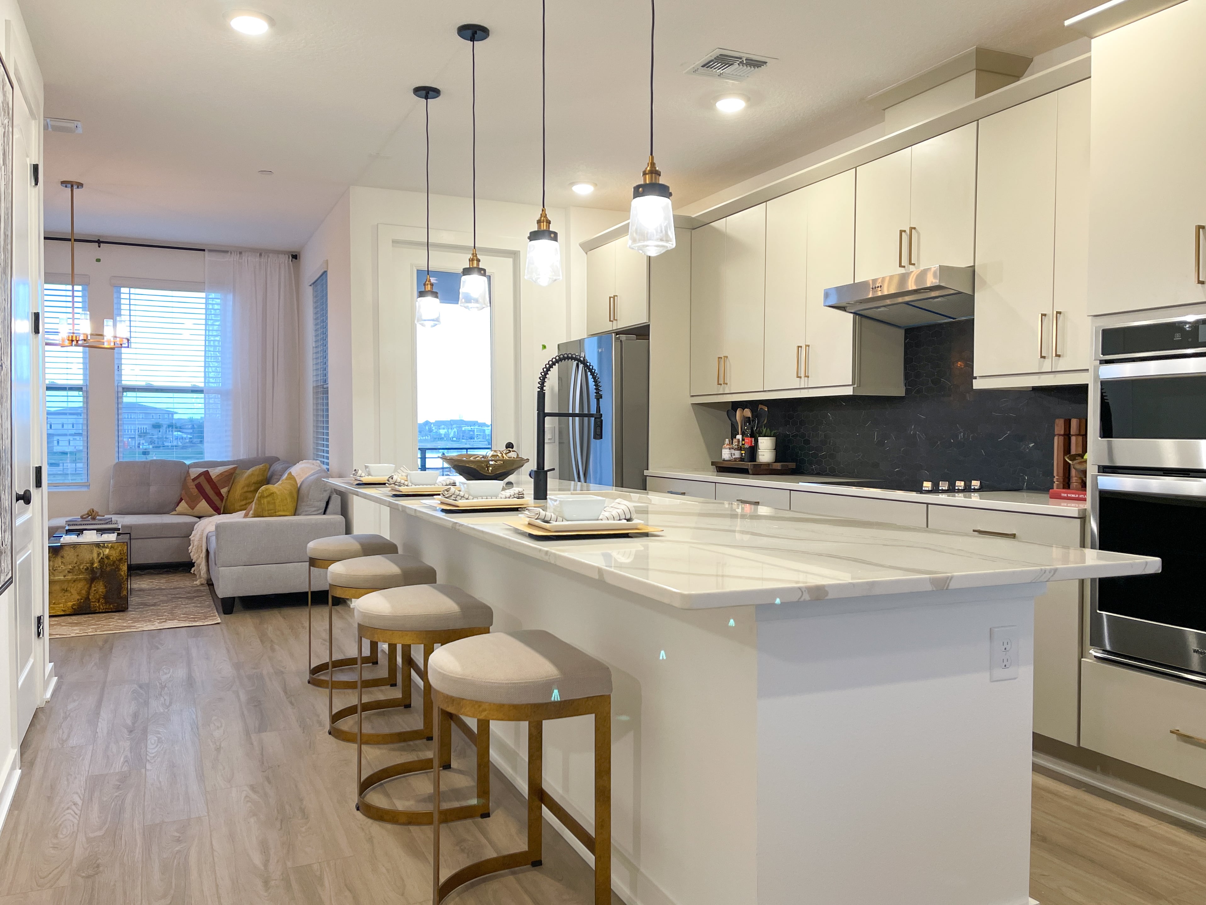 A stylish, turnkey open-concept kitchen with white cabinetry, a large island with marble countertops, and pendant lighting. The kitchen seamlessly transitions into a cozy living space with a neutral color palette and warm accent pieces.