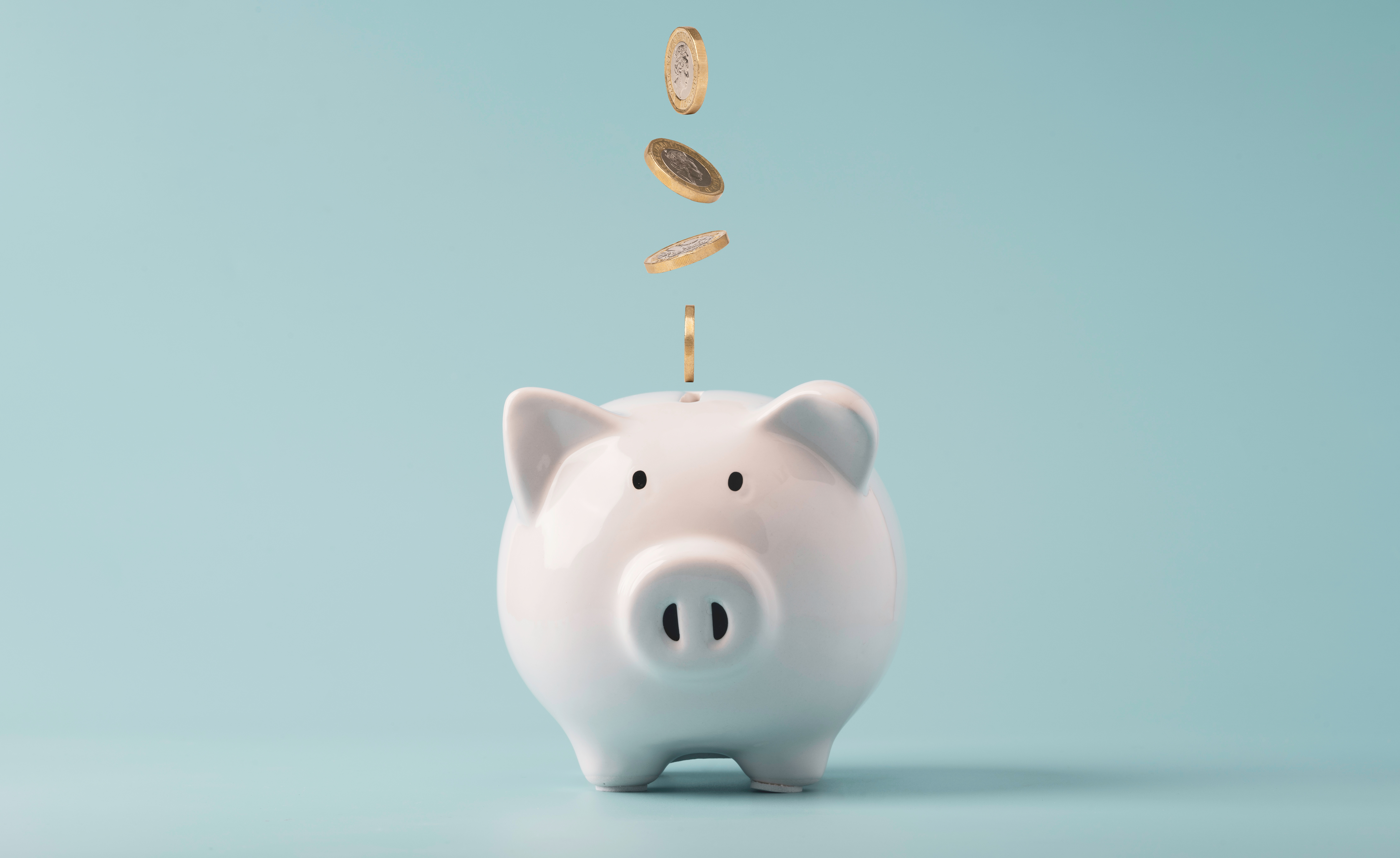 A white piggy bank with coins dropping into it against a light blue background.