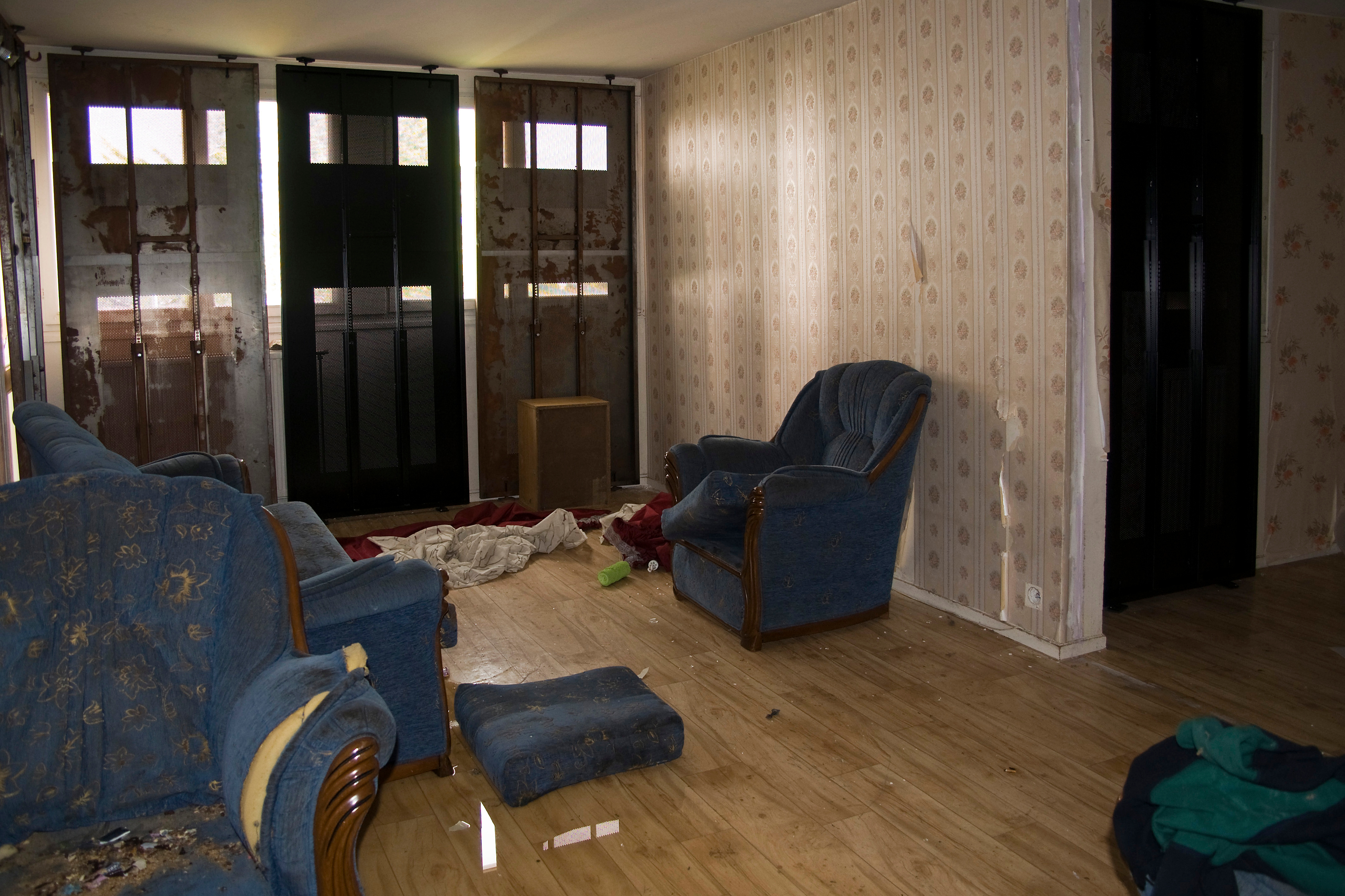 Interior of an abandoned or squatted home with damaged furniture, torn upholstery, stained walls, and scattered debris on a wooden floor—illustrating the impact of unlawful occupancy.