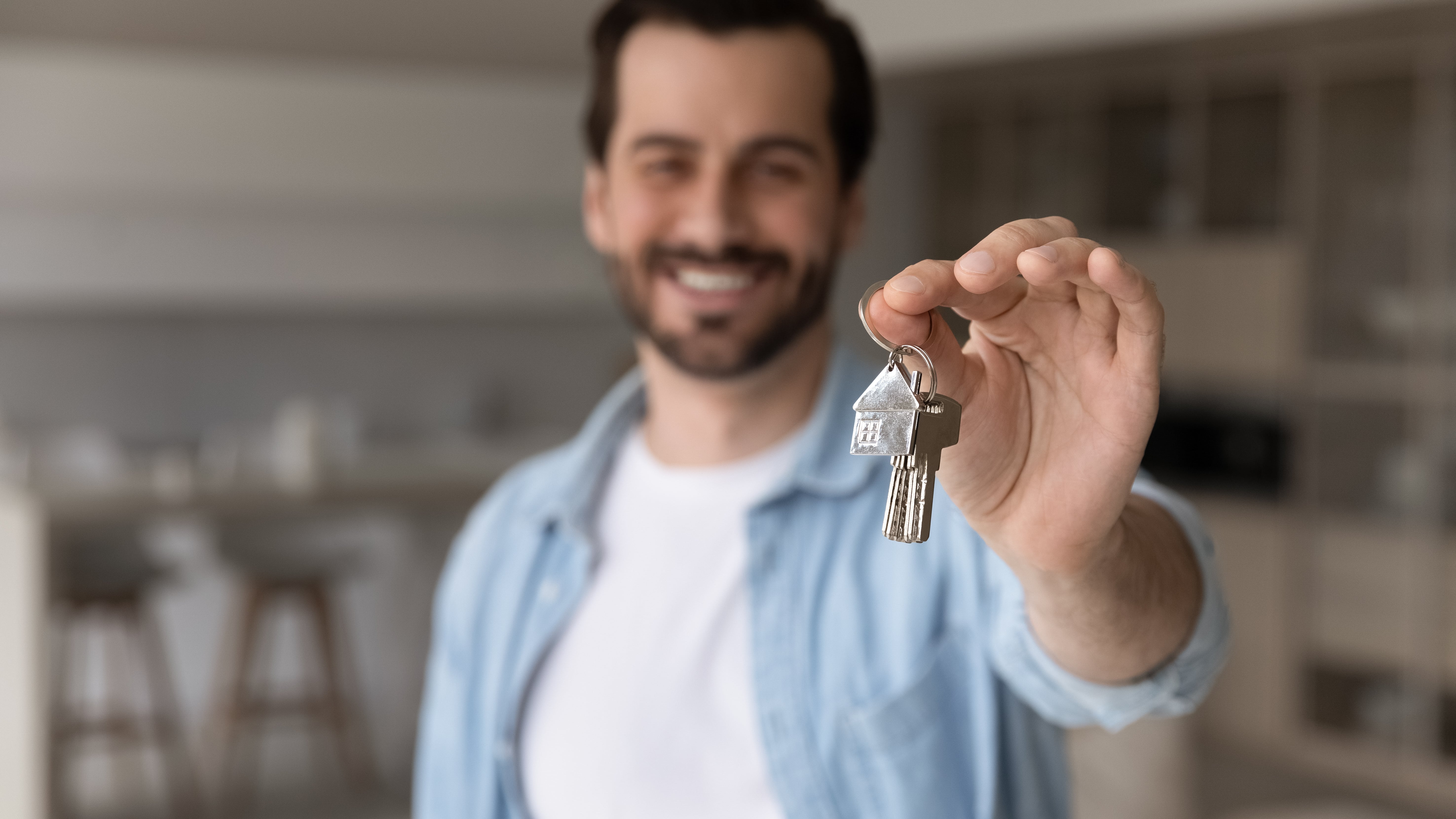 Smiling man holding a house-shaped keychain and keys, standing in a modern kitchen setting, symbolizing new rental approval.