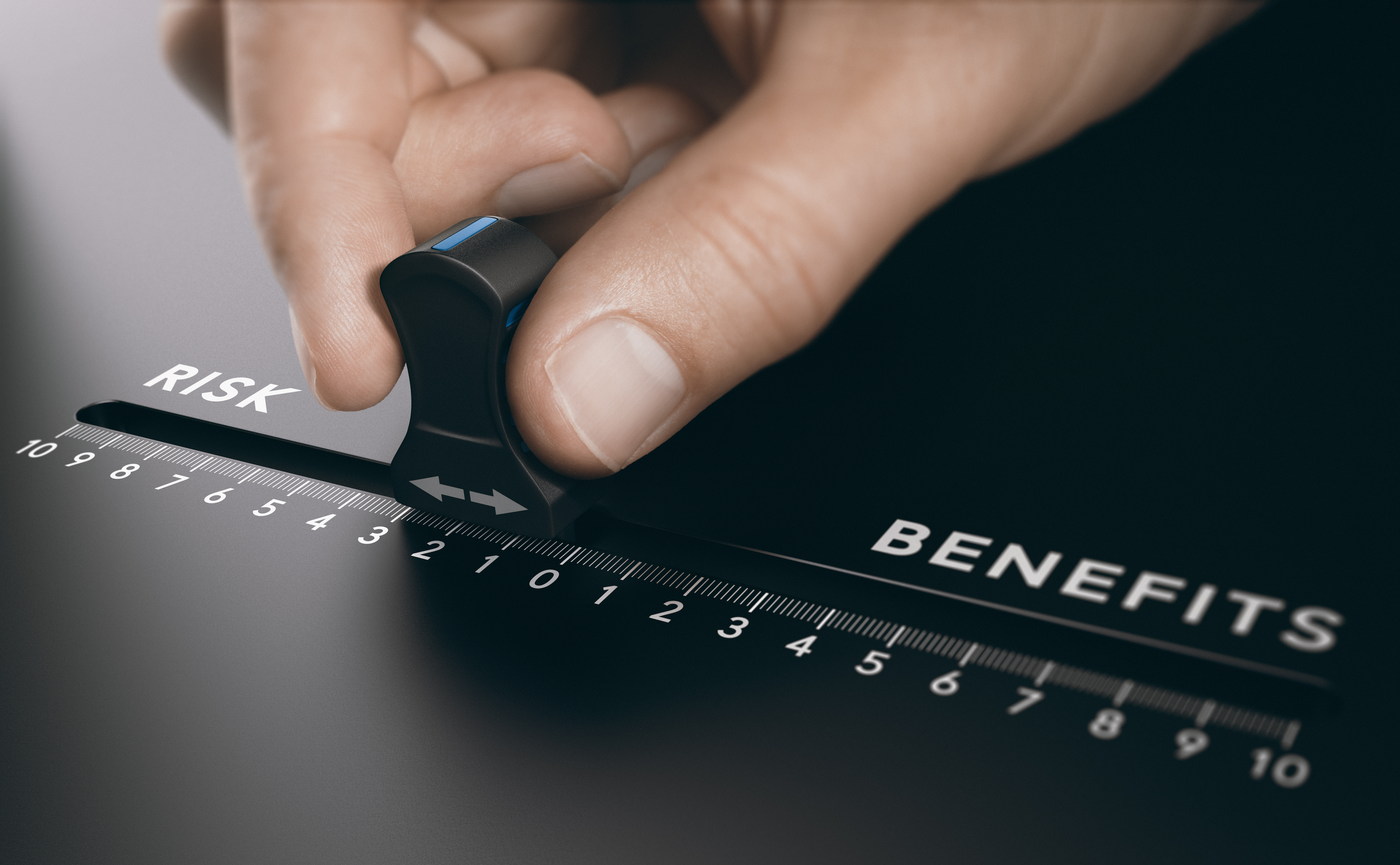 Close-up of a hand adjusting a sliding scale between ‘Risk’ and ‘Benefits,’ representing decision-making, risk management, and strategic planning.