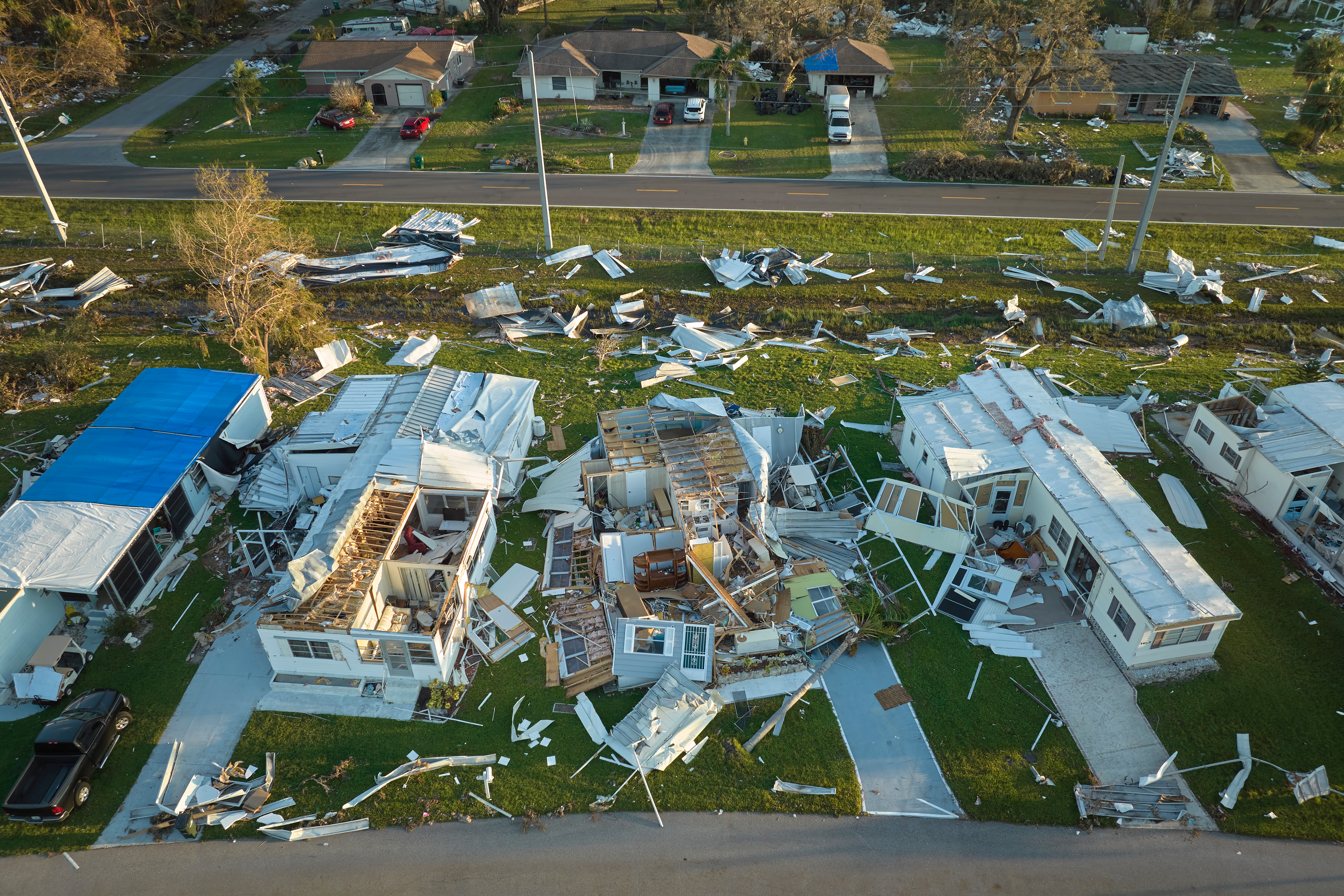 An aerial view of a residential area showing severe hurricane damage. Several homes have been destroyed, with roofs torn off and debris scattered throughout the neighborhood, illustrating the devastating effects of a natural disaster.