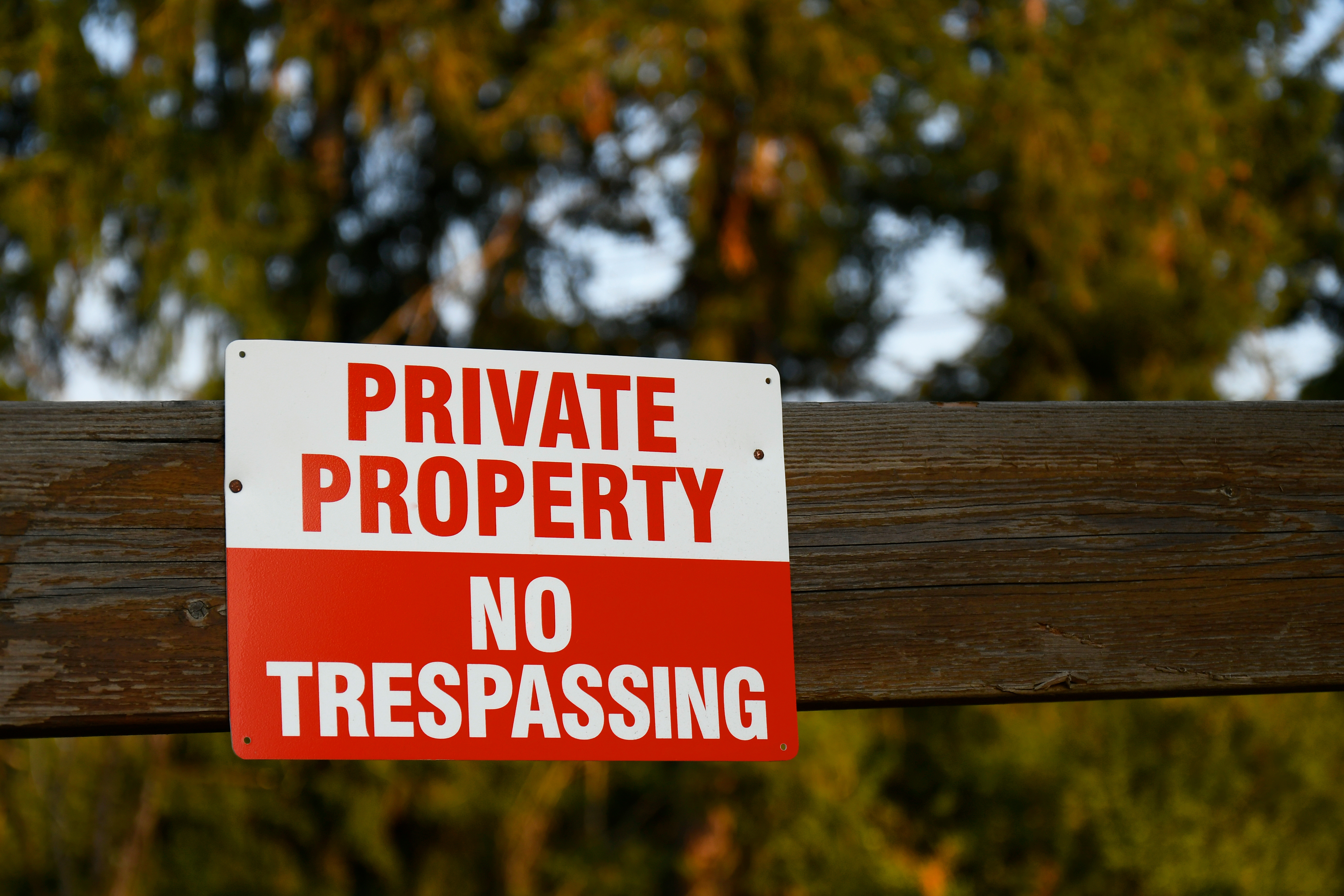 A red and white 'Private Property - No Trespassing' sign mounted on a wooden fence.