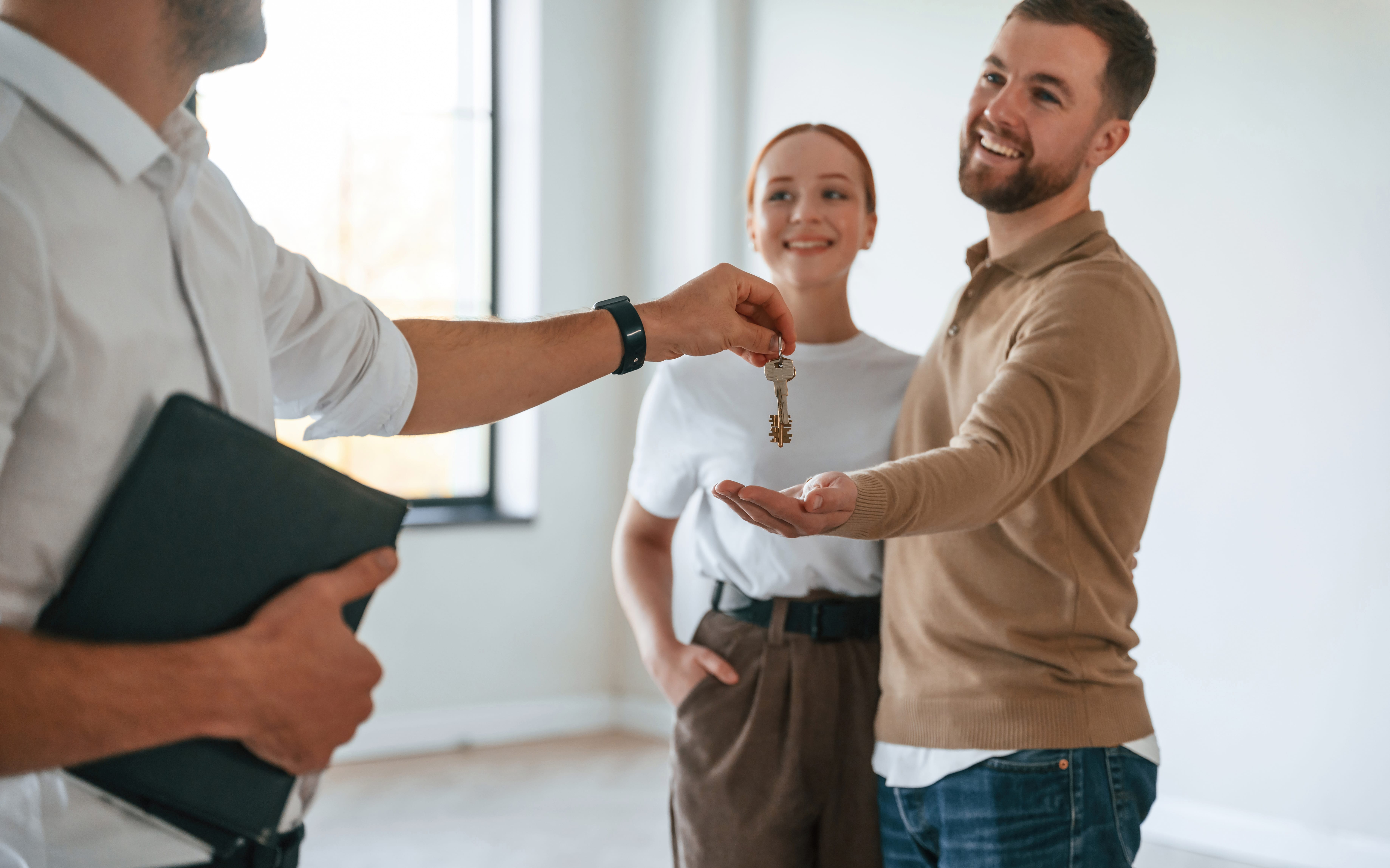 Real estate agent handing over keys to a couple in a bright, modern apartment.