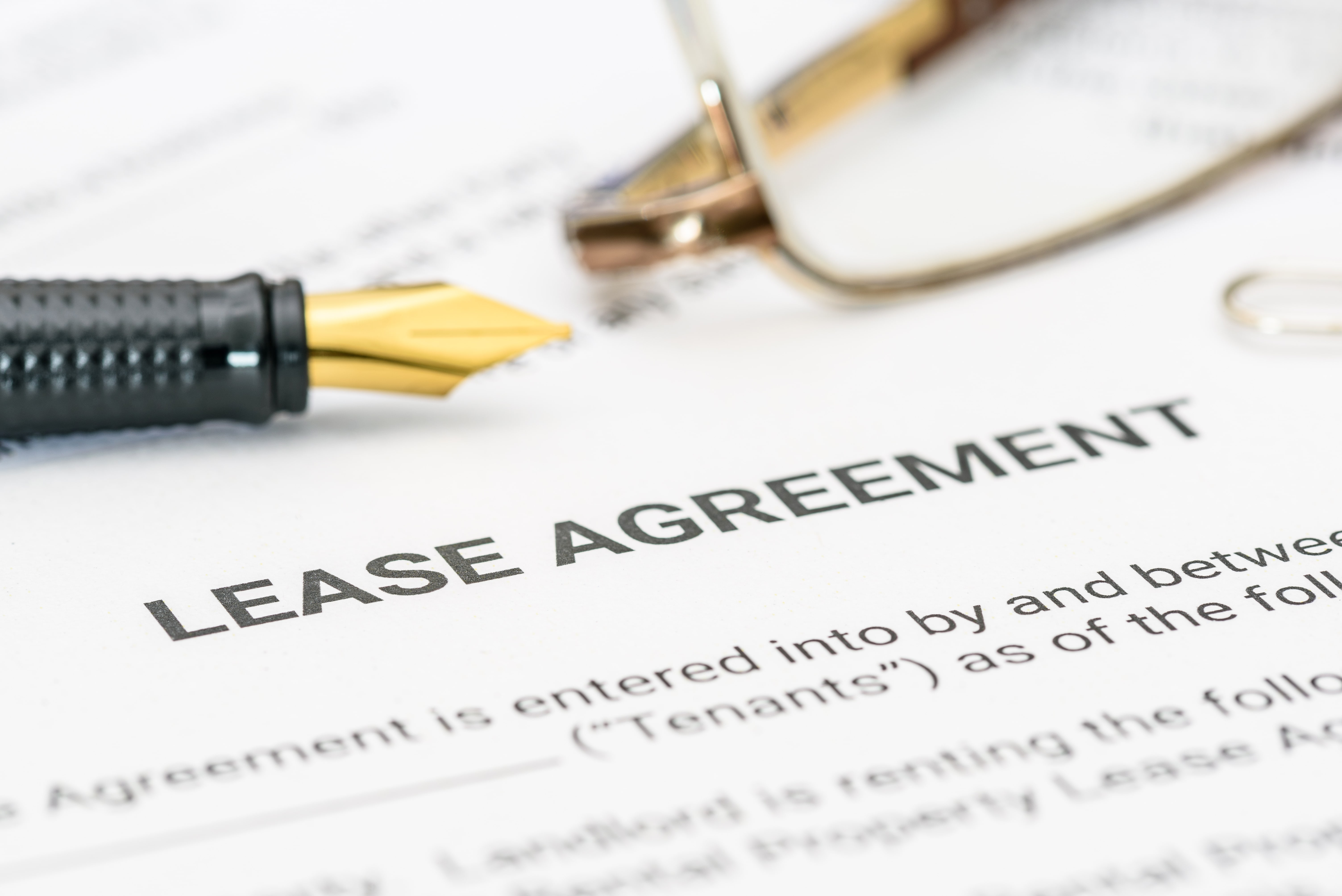 A close-up view of a lease agreement document with a fountain pen and eyeglasses, highlighting the importance of carefully reviewing lease terms before breaking a lease.