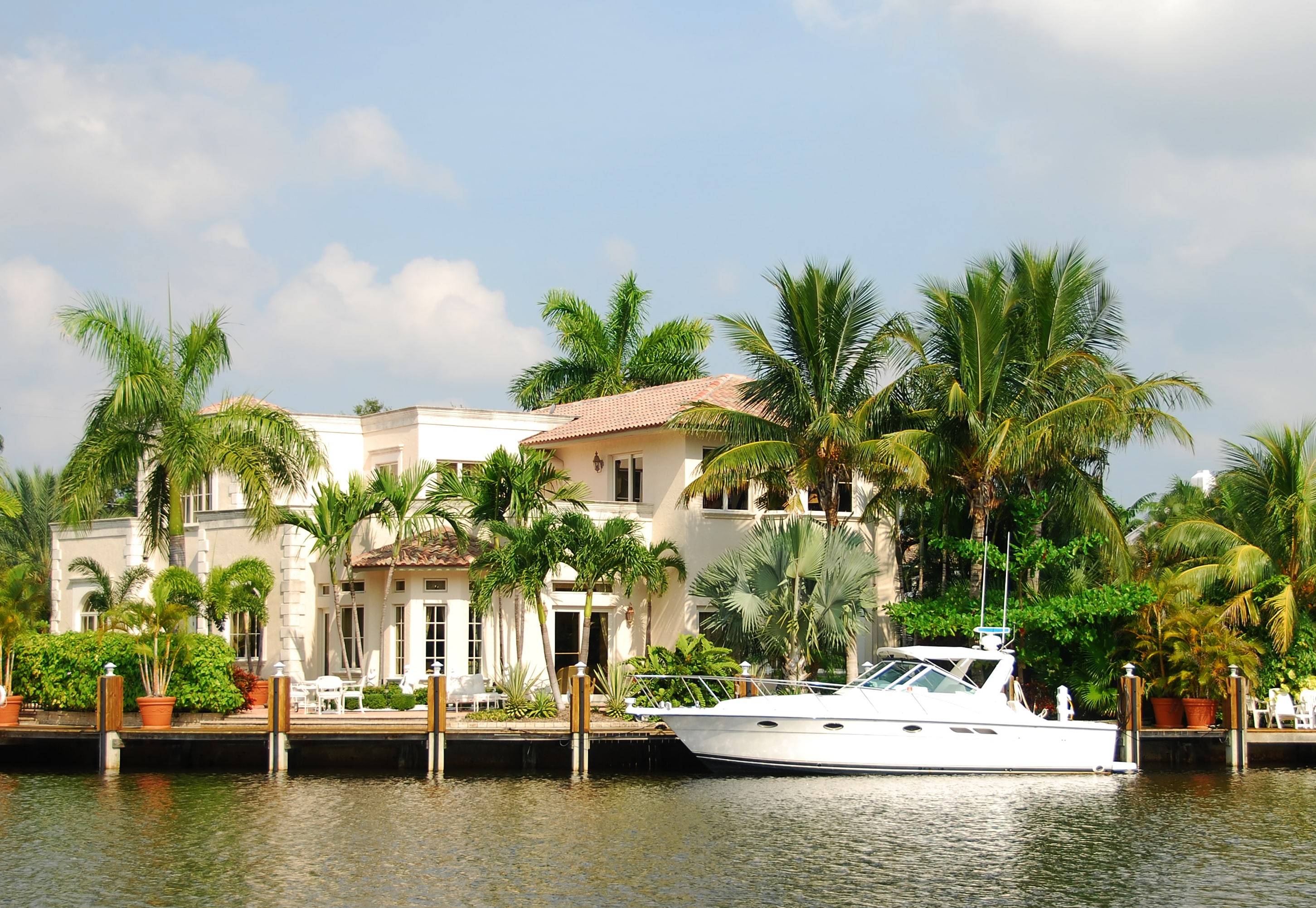 A luxurious waterfront property surrounded by palm trees, with a docked white yacht, showcasing high-value rental real estate.