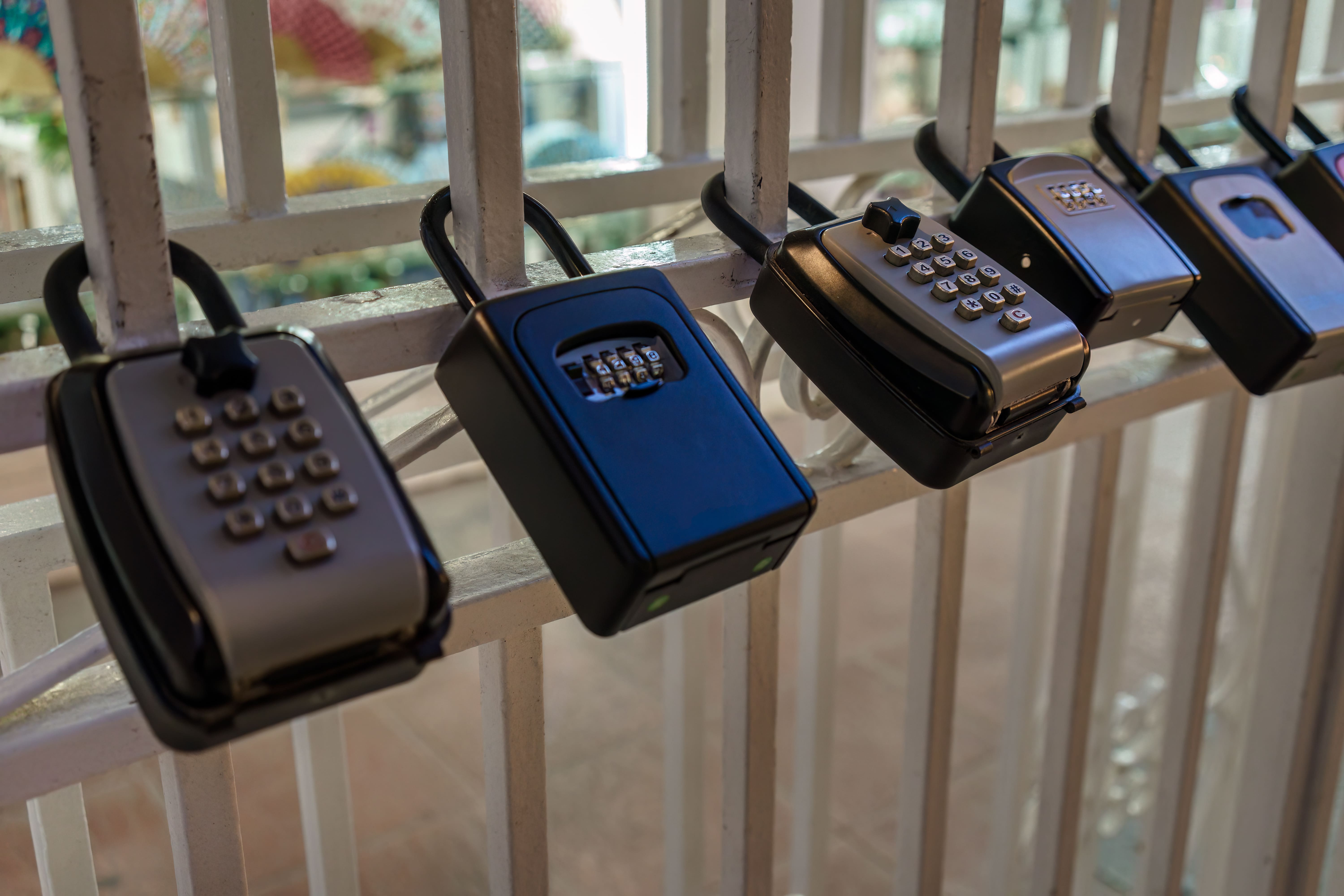 A row of lockboxes secured to a metal gate, used for real estate or property management access.