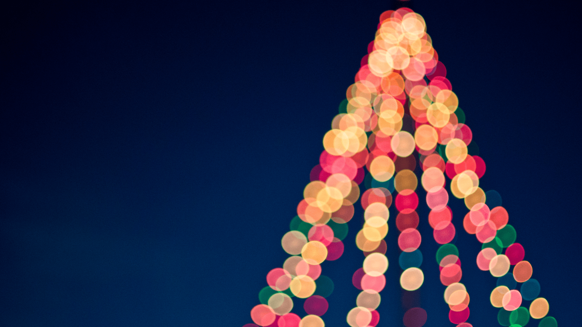 A colorful holiday display with blurred tree lights arranged in the shape of a Christmas tree against a deep blue sky.