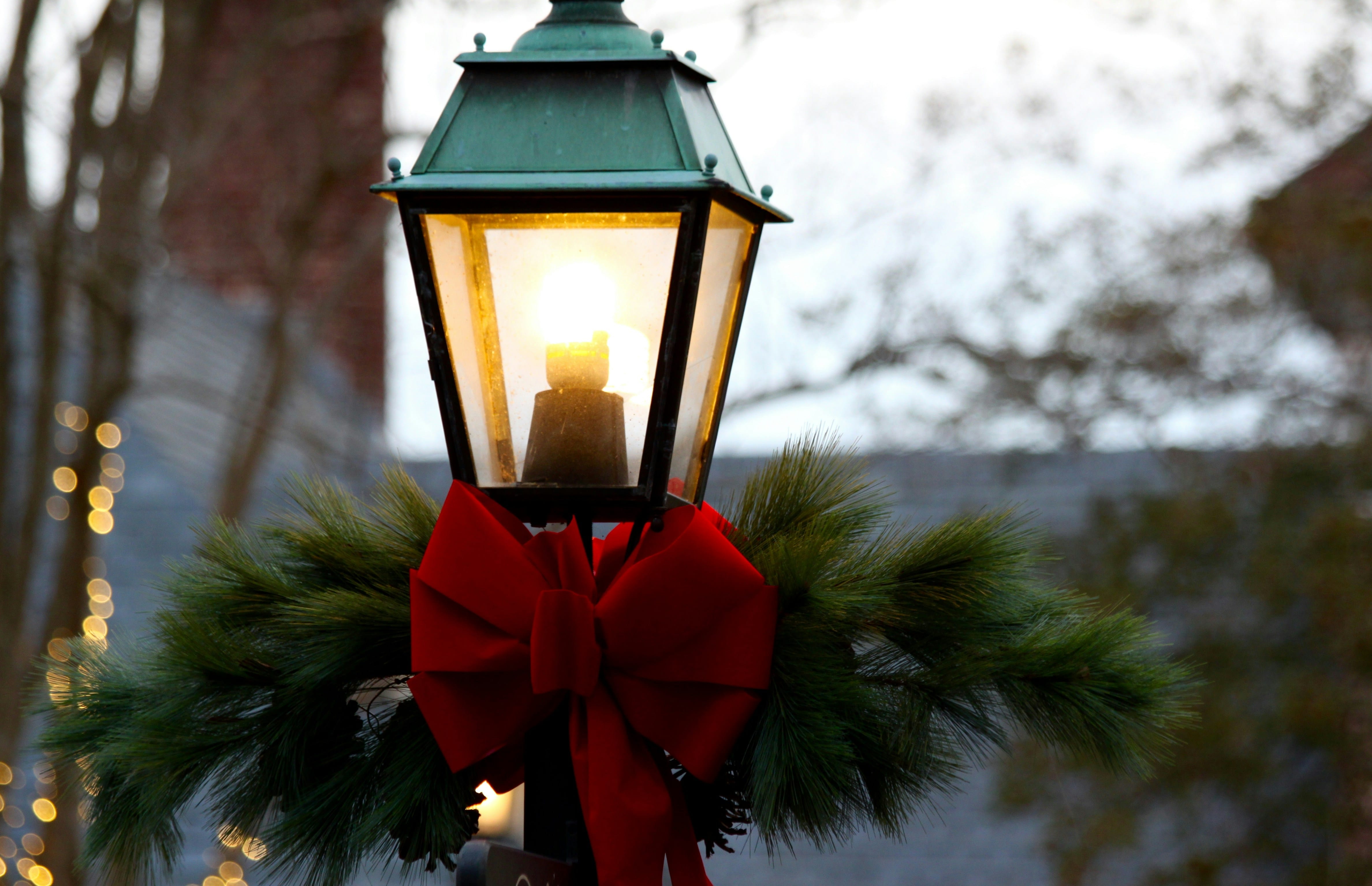 A vintage-style street lamp adorned with pine branches and a red bow, softly glowing against a wintery background. Photo by Josh Harrison on Unsplash